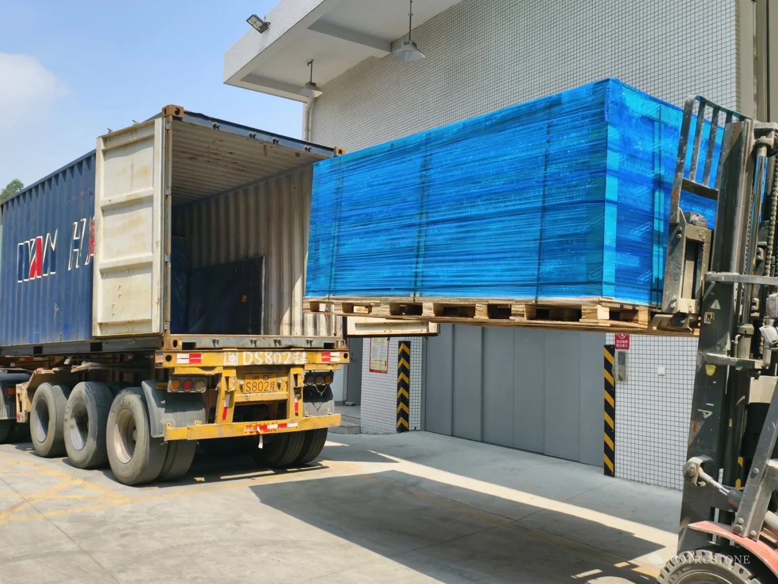 Forklift loading a wrapped stone pallet into an open shipping container