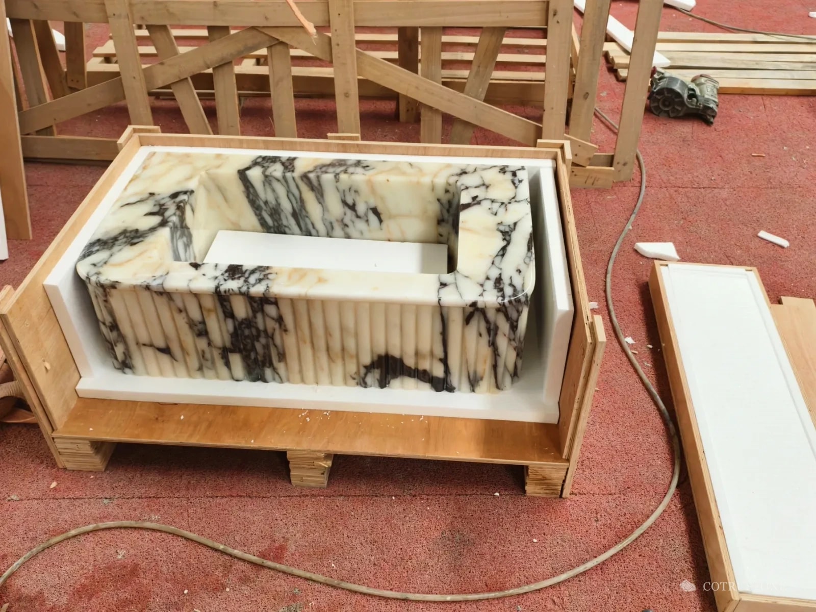 Fluted marble bathtub lined with foam inside an open timber crate