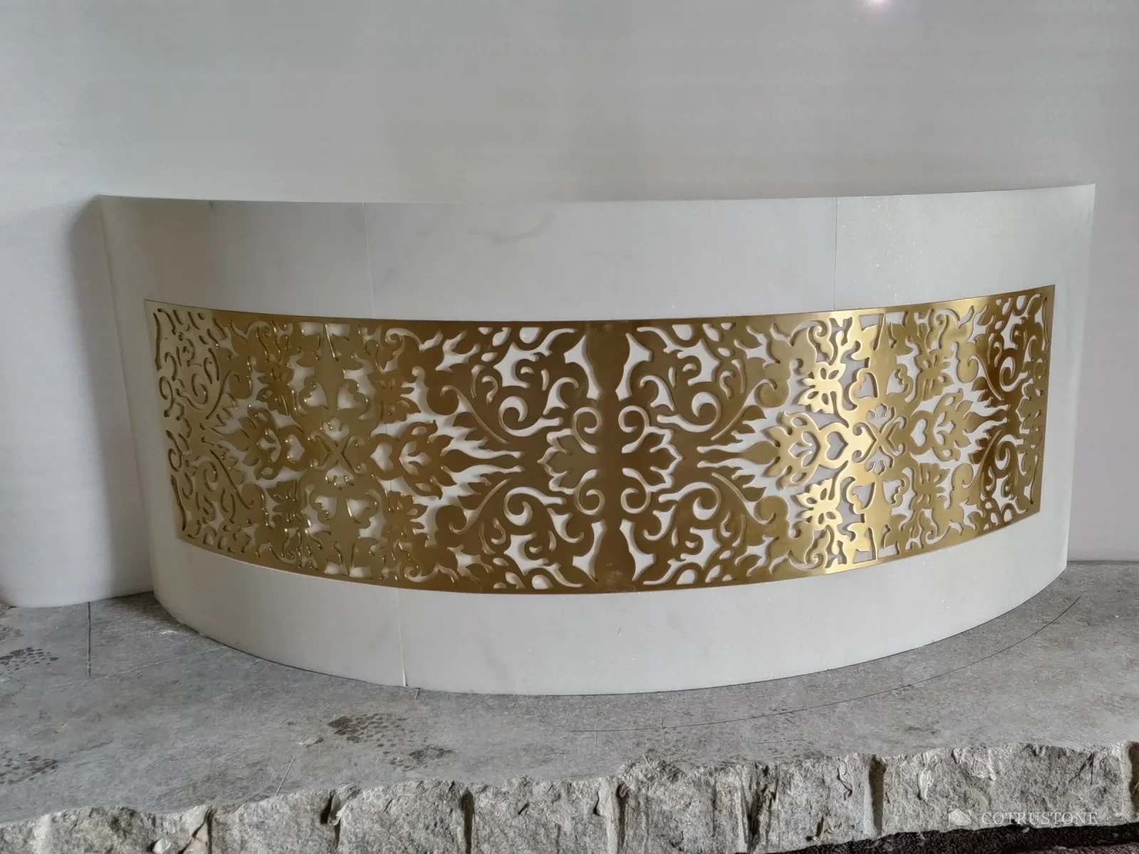 Curved white marble reception counter with a gold brass scroll panel set into its front, in the workshop