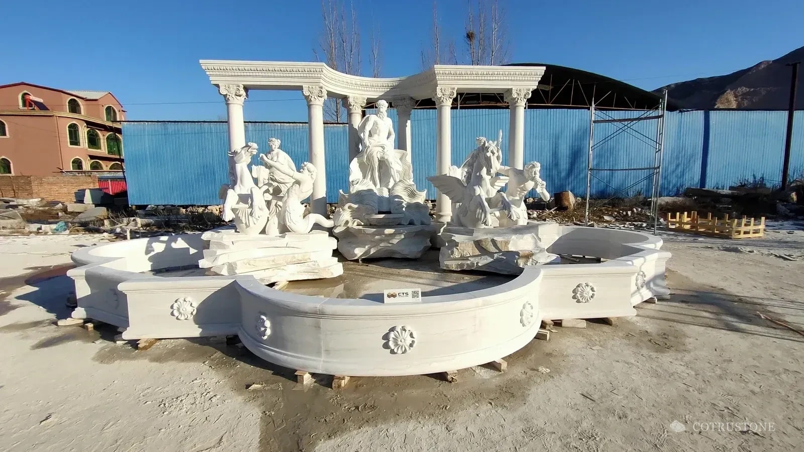White carved fountain with figurative sculptures and a curved colonnade assembled in the workshop yard