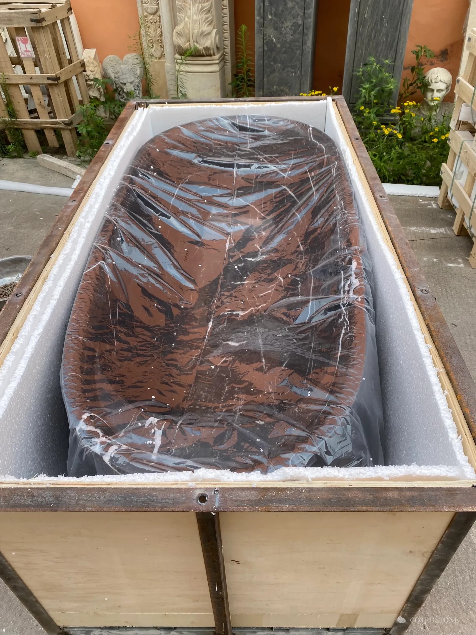 Complete stone bathtub inside an open reinforced timber crate with foam-lined walls