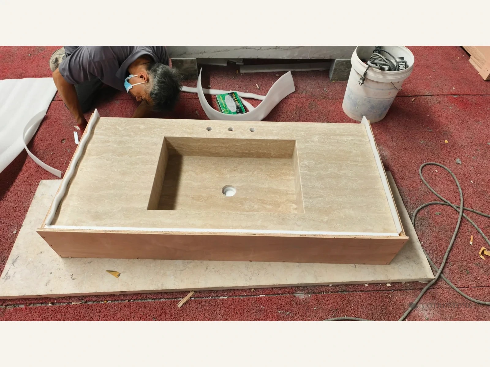 Worker fitting a foam-lined timber crate around a long travertine sink