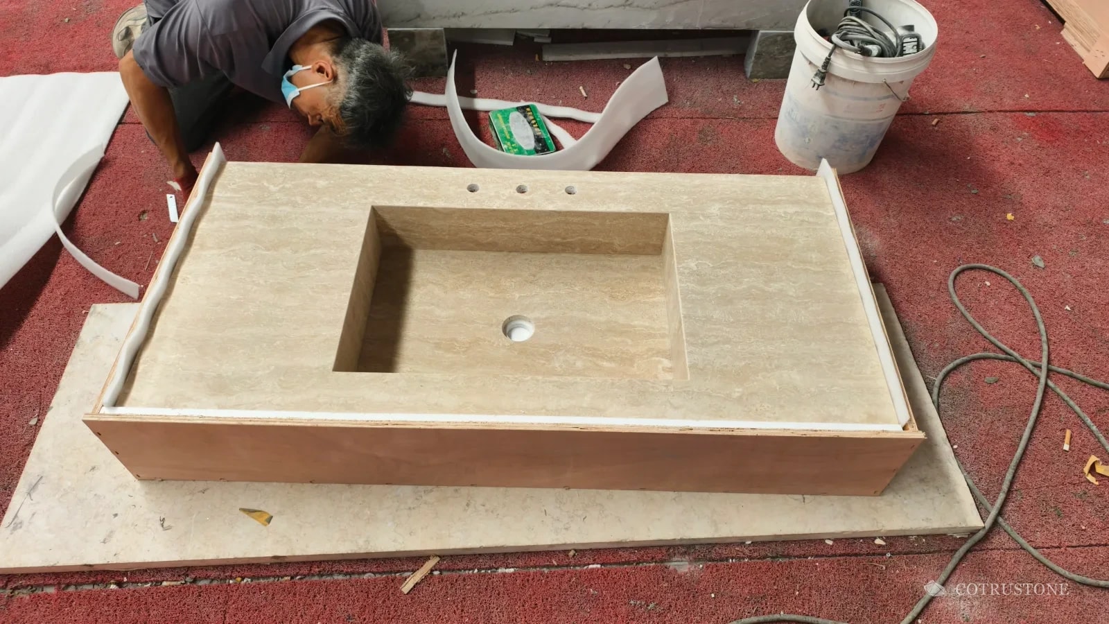 Worker fitting a foam-lined timber crate around a long travertine sink