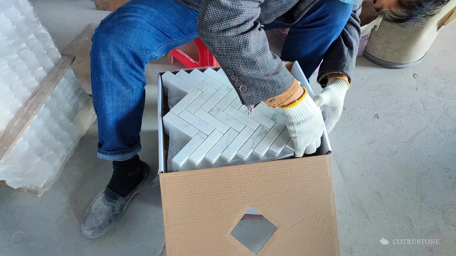 Worker placing herringbone stone mosaic sheets with separating material into a carton
