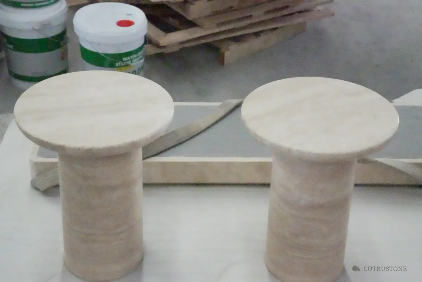 Two pale stone pedestal side tables with circular tops in the workshop