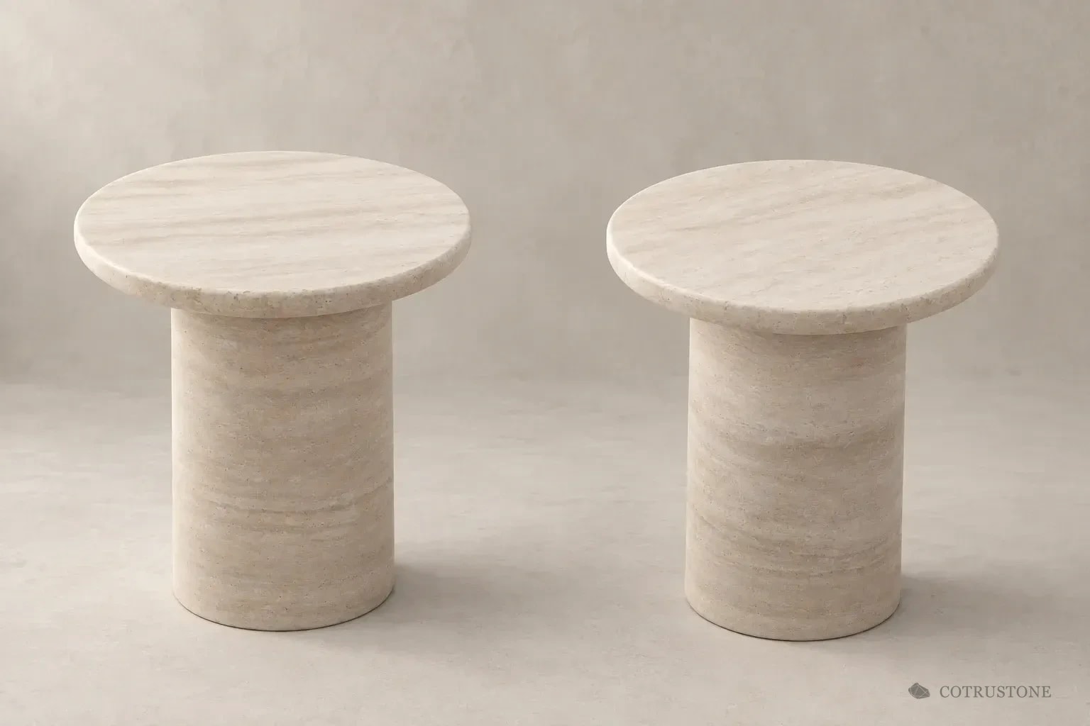 Two pale stone pedestal tables with circular tops in a warm neutral setting