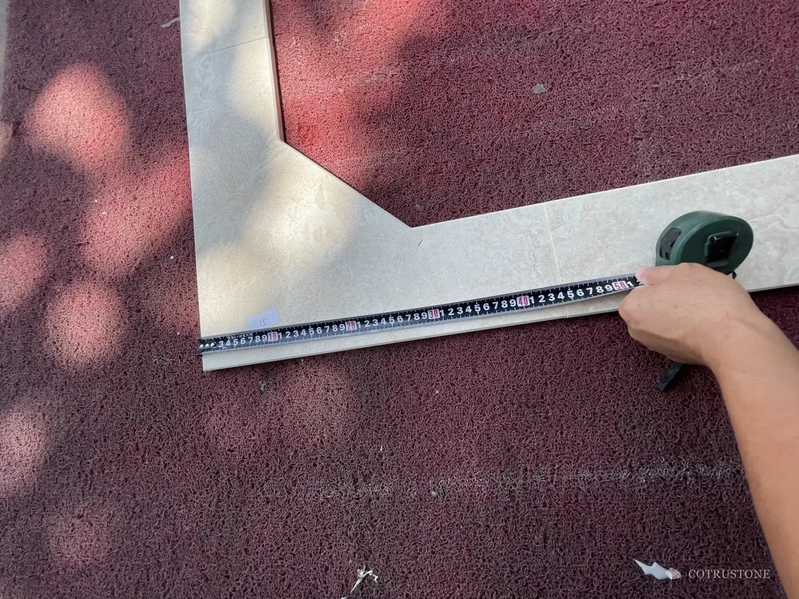 Measuring tape across an angled stone pool surround component during a workshop check
