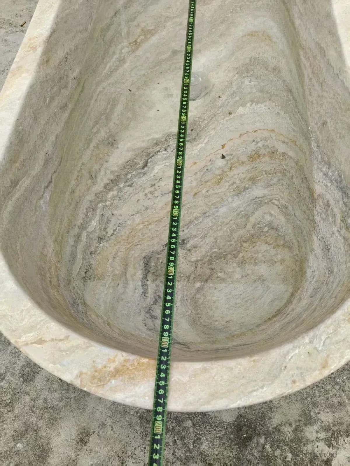 Tape measure across the inside of a silver-toned stone bathtub
