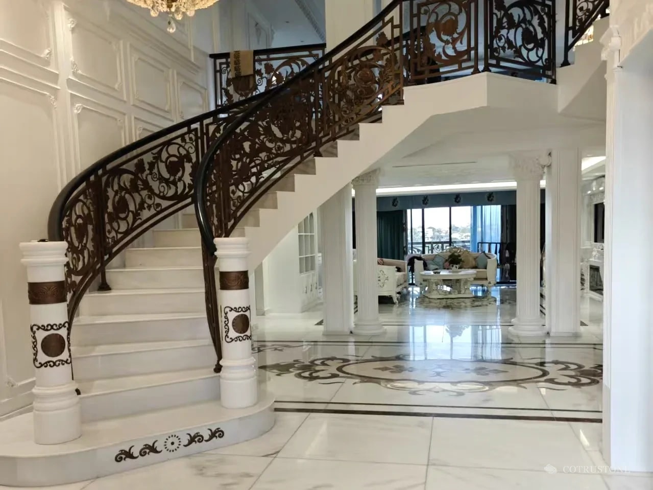 Installed marble staircase with curved first steps, stone newel posts and coordinated floor inlay