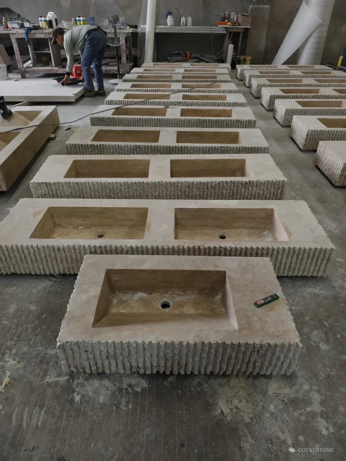 Rows of double-bowl travertine vanity basins during production