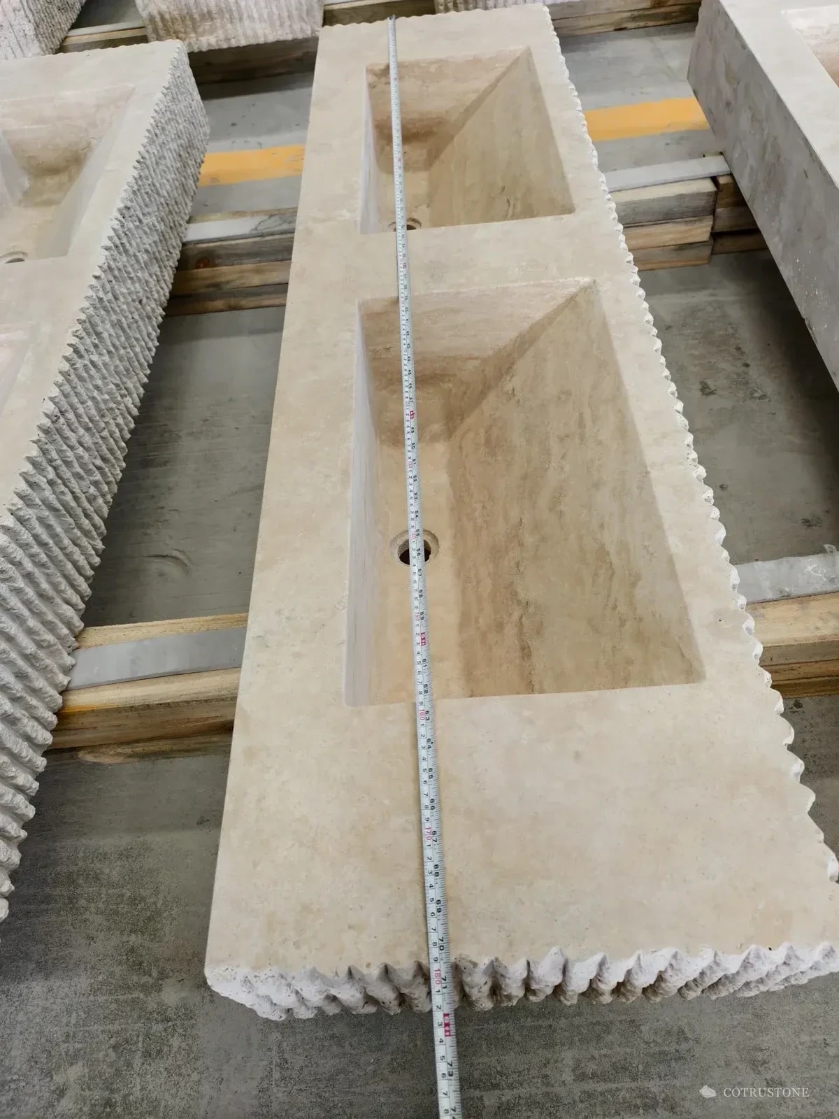 Tape measure across a double-bowl travertine basin during dimensional checking