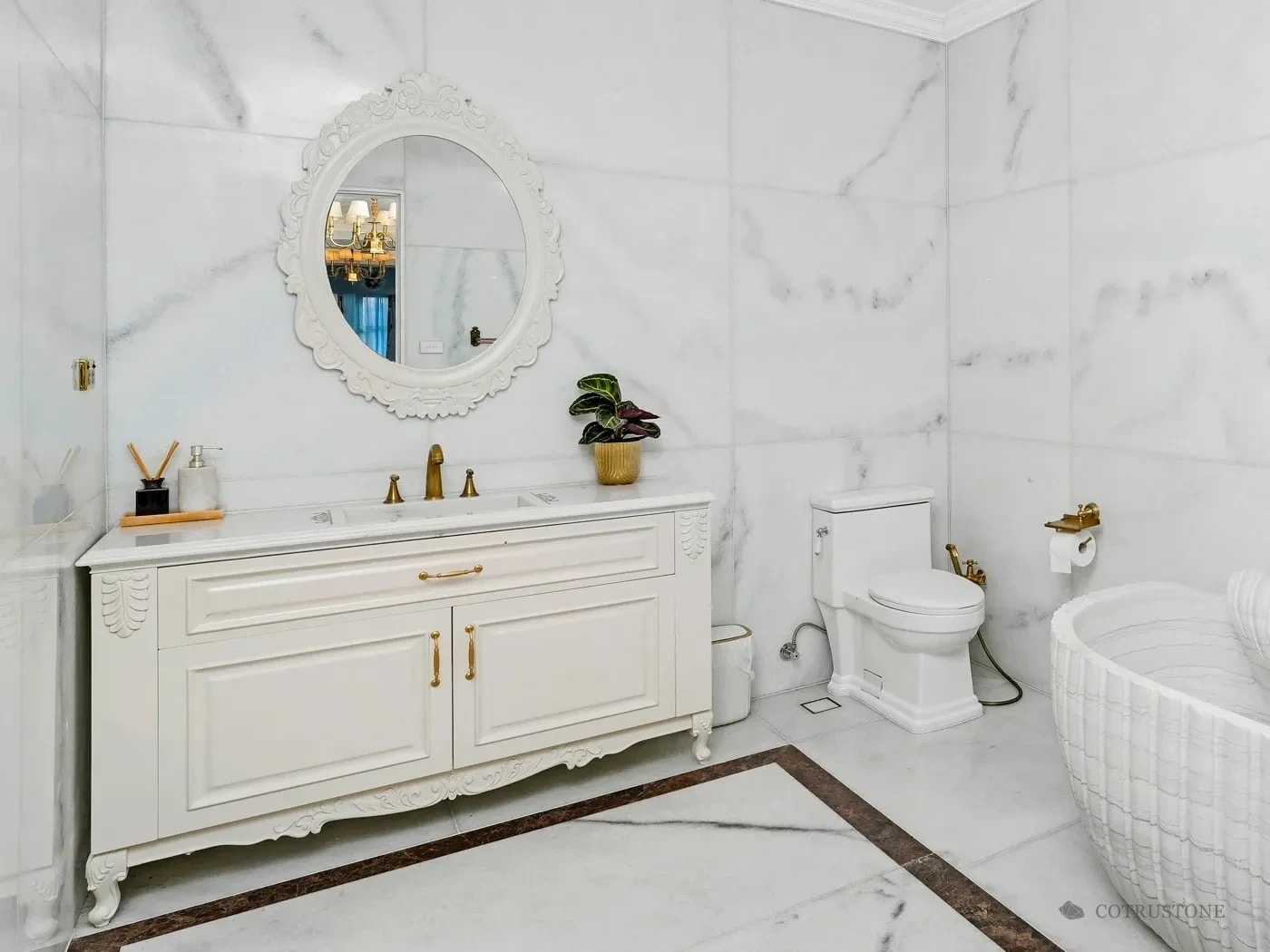 Vanity with a white marble top below an oval mirror, in a bathroom with marble walls and an inlaid marble floor