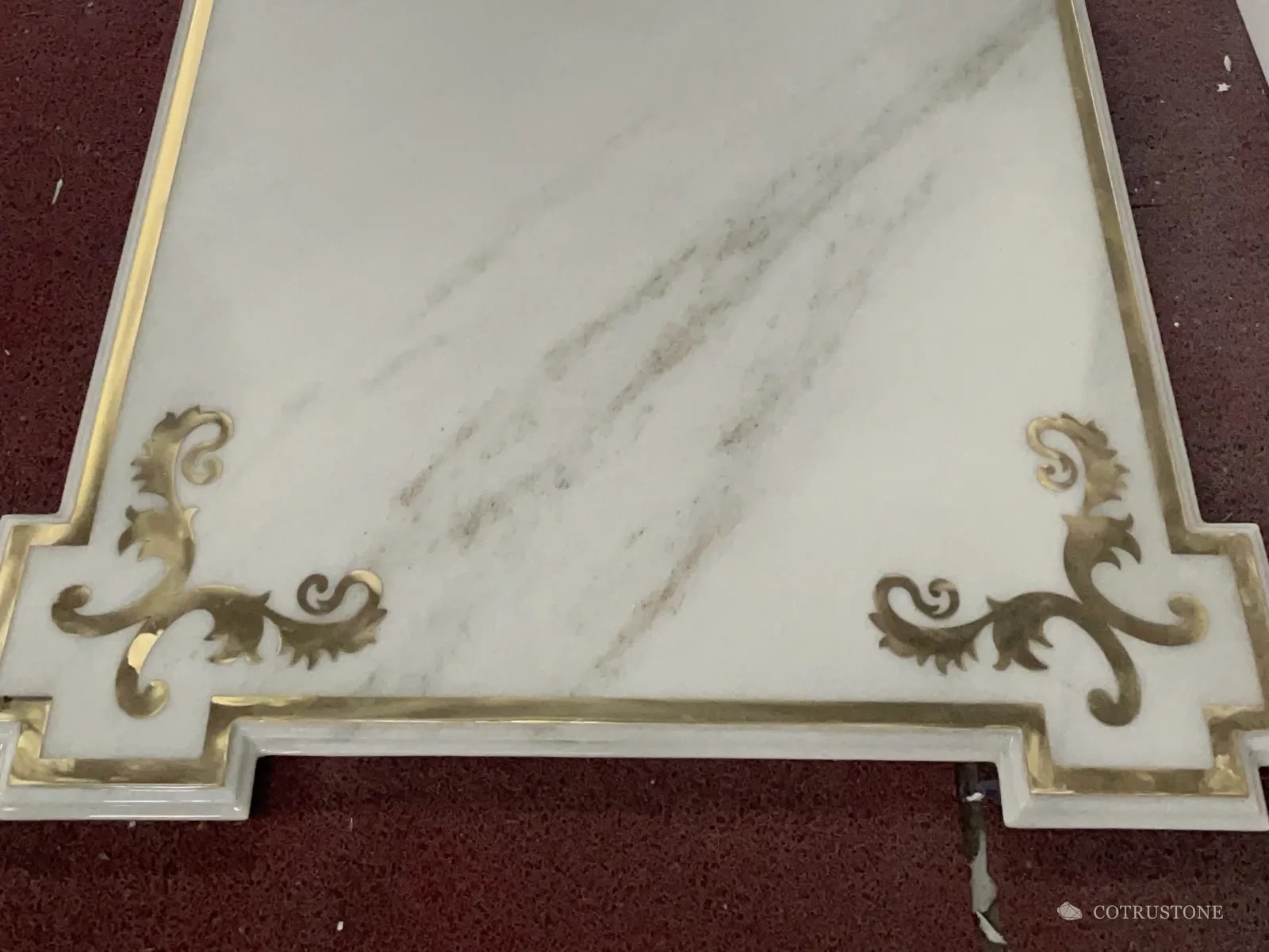 White marble panel with a brass border and brass corner scrolls set into the stone