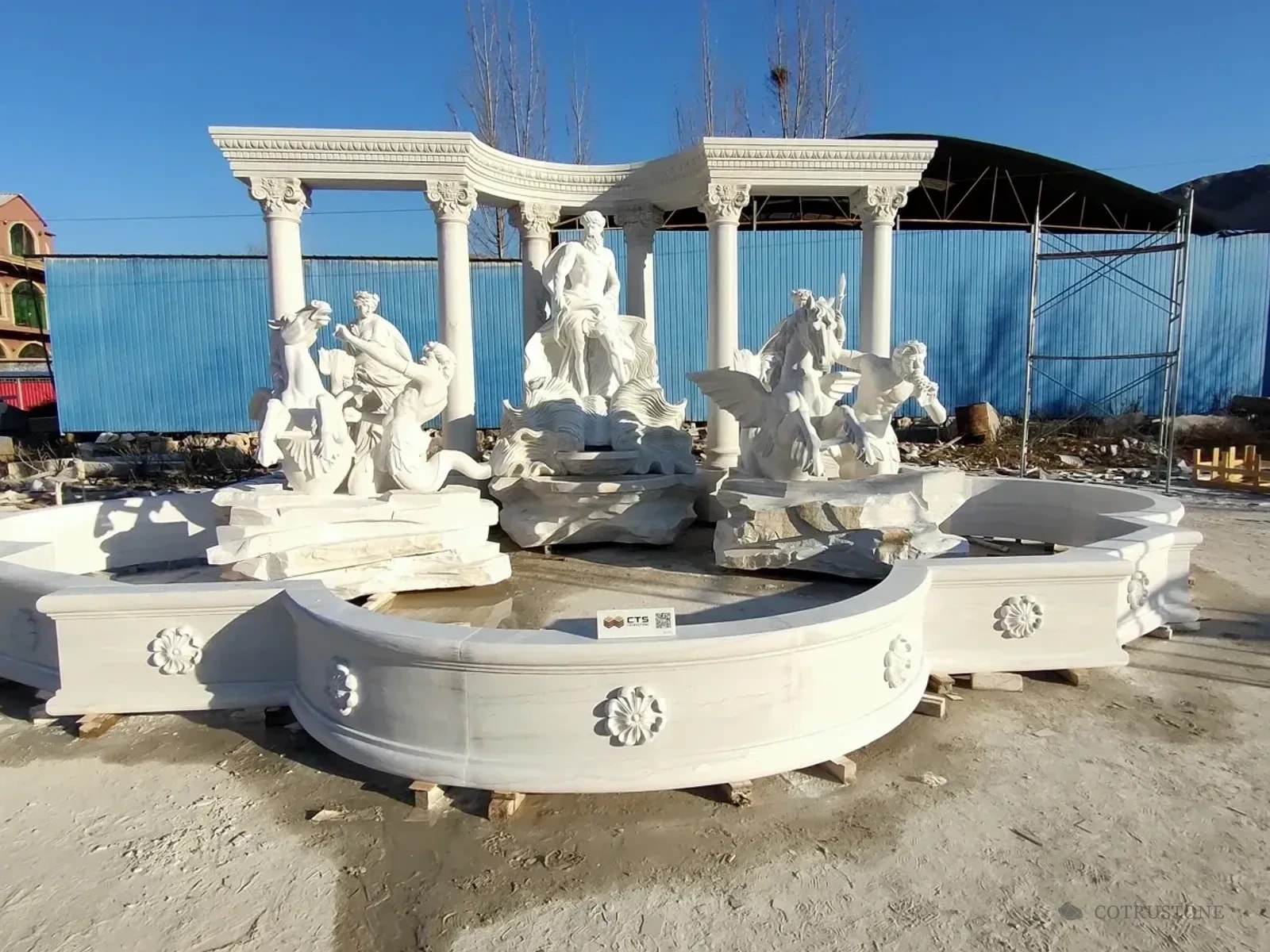 White carved fountain with figurative sculptures and a curved colonnade assembled in the workshop yard