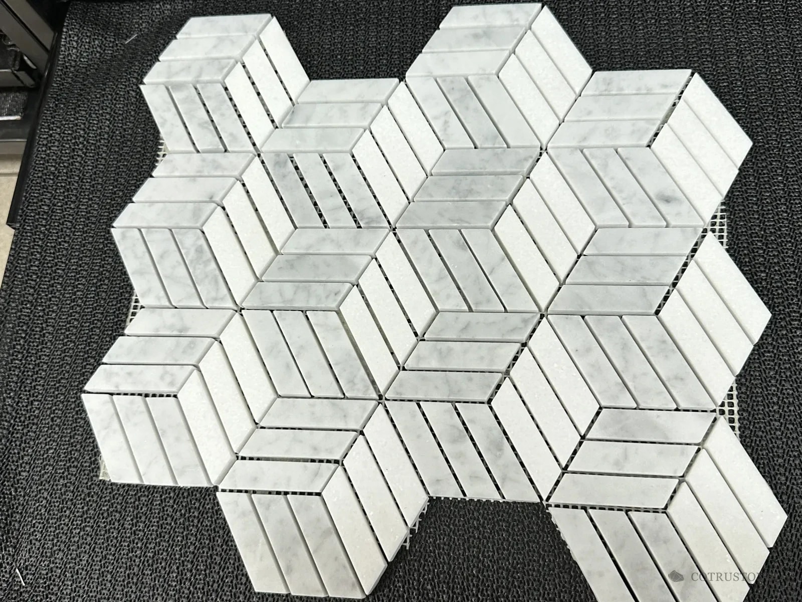 Mosaic sheet of white and grey stone strips forming a three-dimensional cube pattern