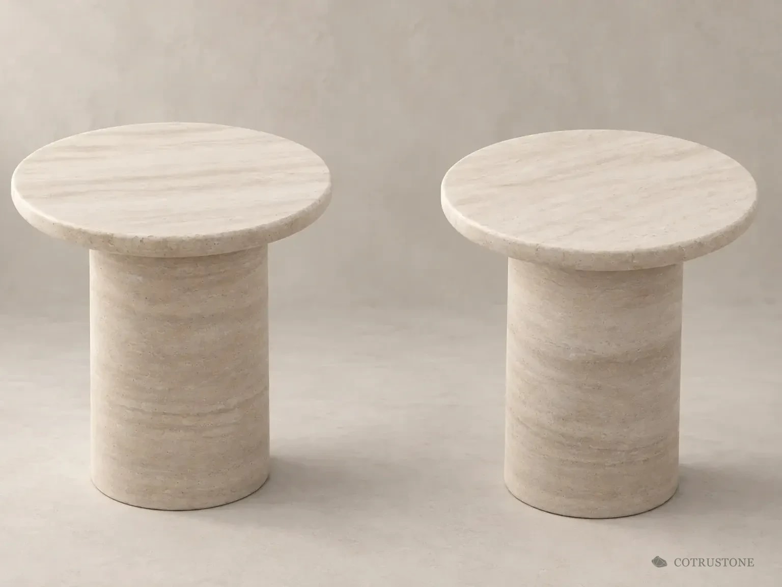 Two pale stone pedestal tables with circular tops in a warm neutral setting