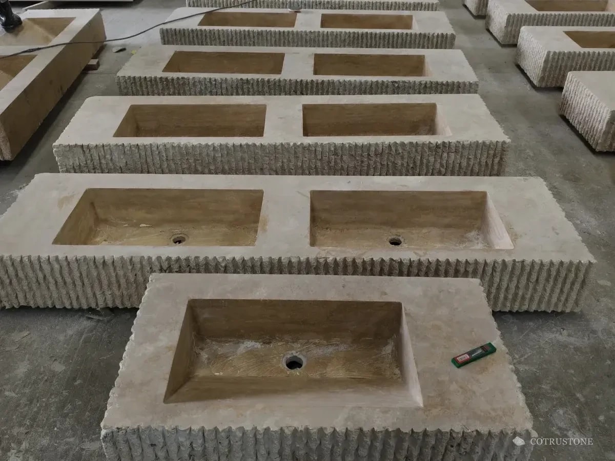 Rows of double-bowl travertine vanity basins during production